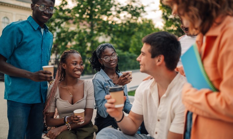 Diverse cheerful students with coffee chatting during a break at campus